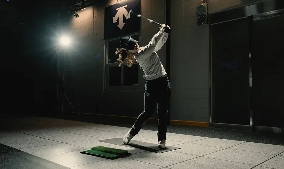 Golfer swinging a club while being tracked in a dark motion capture volume.